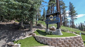 A sign for the Mammoth Mountain Ski & Racquet Club with a stone wall and grass in the foreground.