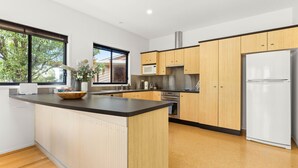 A modern kitchen with wooden cabinets, a central island, a built-in oven, and a refrigerator. - Blue Point House by Experience Jervis Bay (Vincentia)