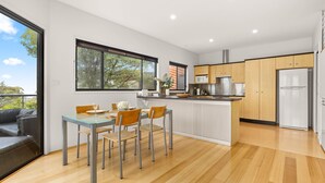 A modern kitchen with wooden cabinets, a central island, and a built-in oven. - Blue Point House by Experience Jervis Bay (Vincentia)