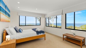 A bedroom with a bed, bedside tables, a bench, and large windows offering ocean views. - Blue Point House by Experience Jervis Bay (Vincentia)