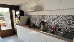 A modern kitchen with white cabinets, a stainless steel sink, and patterned backsplash tiles. - Maison de Ville (Cambrai)