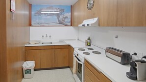 Una cocina compacta con armarios de madera, una encimera blanca, una hornilla, un tostador y un reloj de pared.