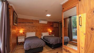A wooden-paneled room with two beds, nightstands, a wall-mounted air conditioner, and a window with curtains.