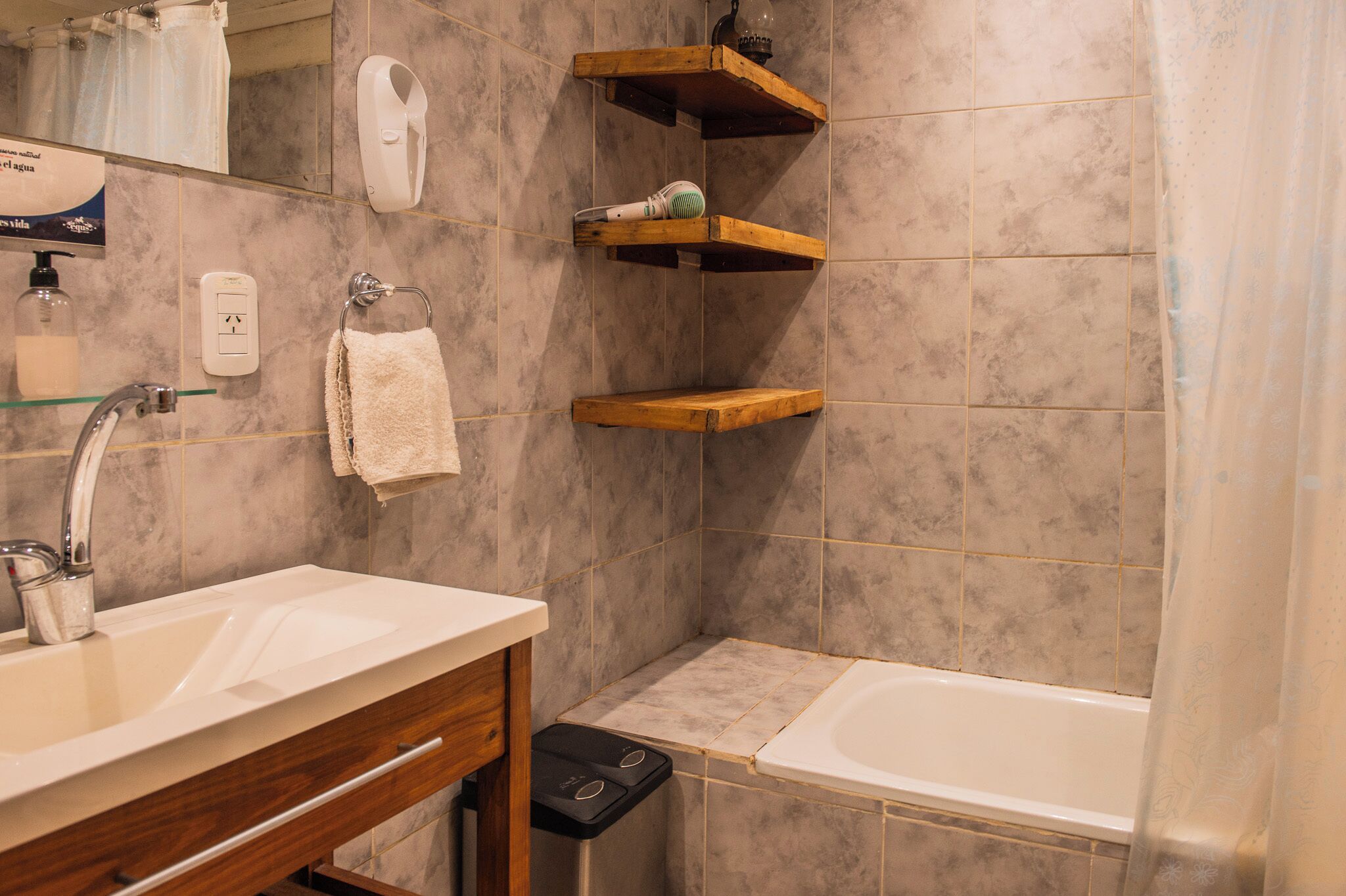 A bathroom with a sink, mirror, towel rack, shower, and wooden shelves.