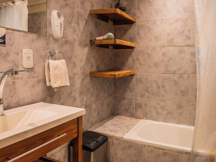 A bathroom with a sink, mirror, towel rack, shower, and wooden shelves.