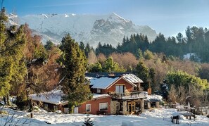 A chalet with a balcony, surrounded by snow-covered trees and mountains in the background. - Equs Posada de Campo (San Carlos de Bariloche)