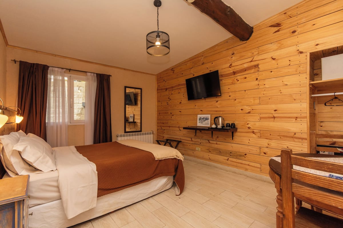 A wooden-paneled room with a bed, a television, and a small table with a kettle.
