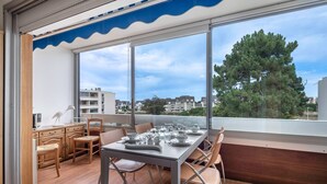 A modern dining area with a table set for four, large windows, and a view of buildings and trees. - 500m from the beach, flat for 2 (La Baule-Escoublac)