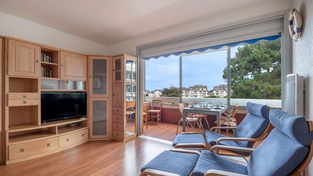 A spacious living area with a flat-screen TV, wooden cabinets, and a balcony with blue cushioned chairs. - 500m from the beach, flat for 2 (La Baule-Escoublac)