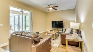 A living room with a leather sofa, a coffee table, a TV, and a ceiling fan. - 5 Mi to Weeki Wachee Springs! Poolside Retreat (Brooksville)