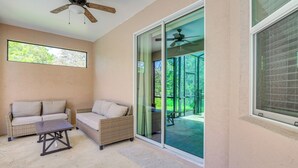 A covered patio area with a ceiling fan, a wicker sofa, a small table, and a sliding glass door leading to an outdoor space. - 5 Mi to Weeki Wachee Springs! Poolside Retreat (Brooksville)