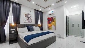 A modern bedroom with a large bed, dark curtains, a ceiling light, a wall-mounted air conditioner, and a wardrobe. - Benetton Apt - Pure elegance (Lekki, Lagos State, Nigeria)