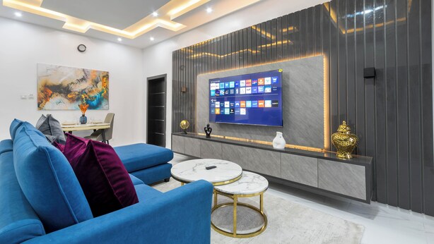 A modern living room with a blue sofa, two marble coffee tables, a flat-screen TV, and a decorative wall panel. - Benetton Apt - Pure elegance (Lekki, Lagos State, Nigeria)