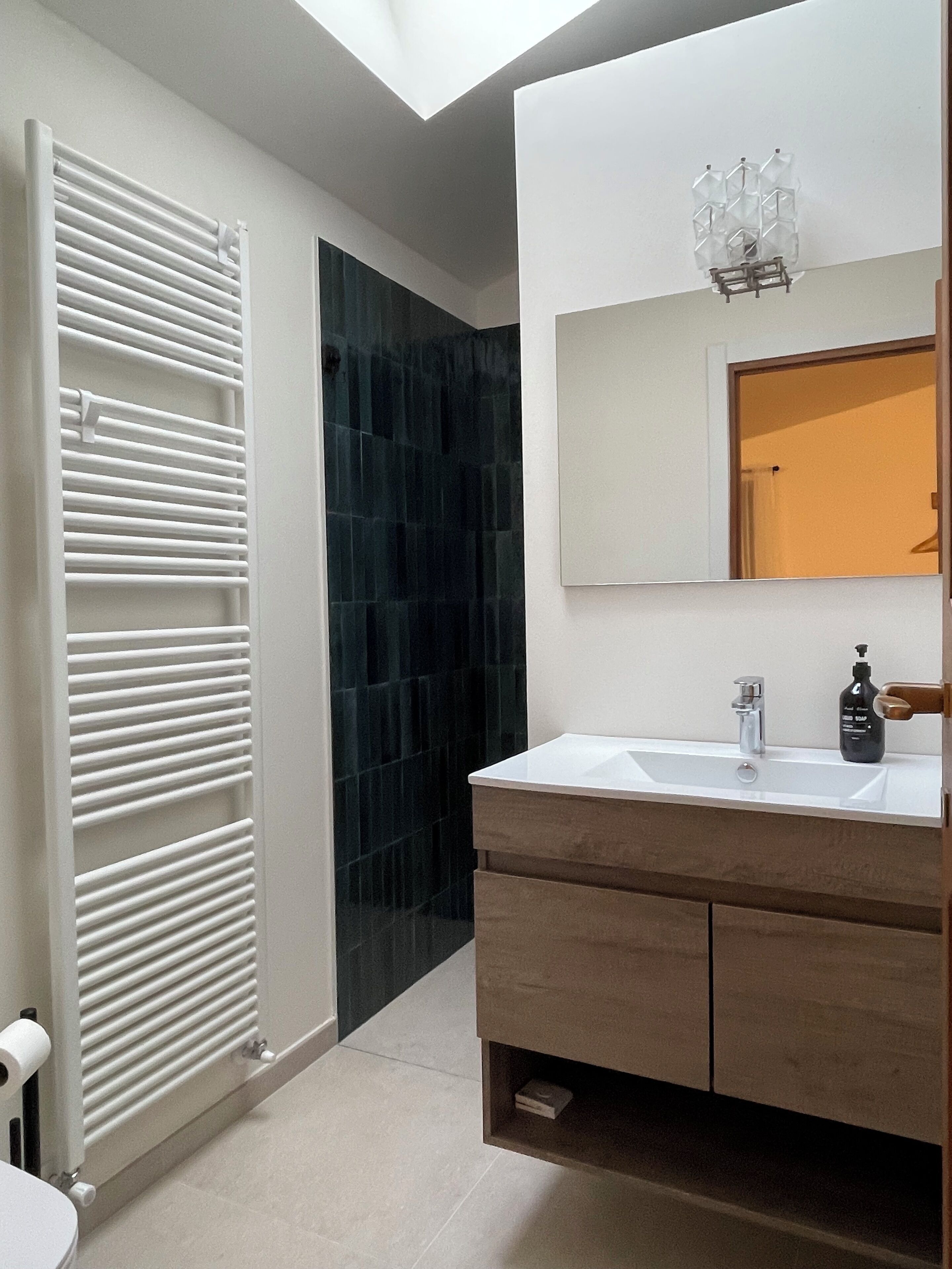 A modern bathroom with a white radiator, dark tiled wall, and a vanity with a mirror and sink.