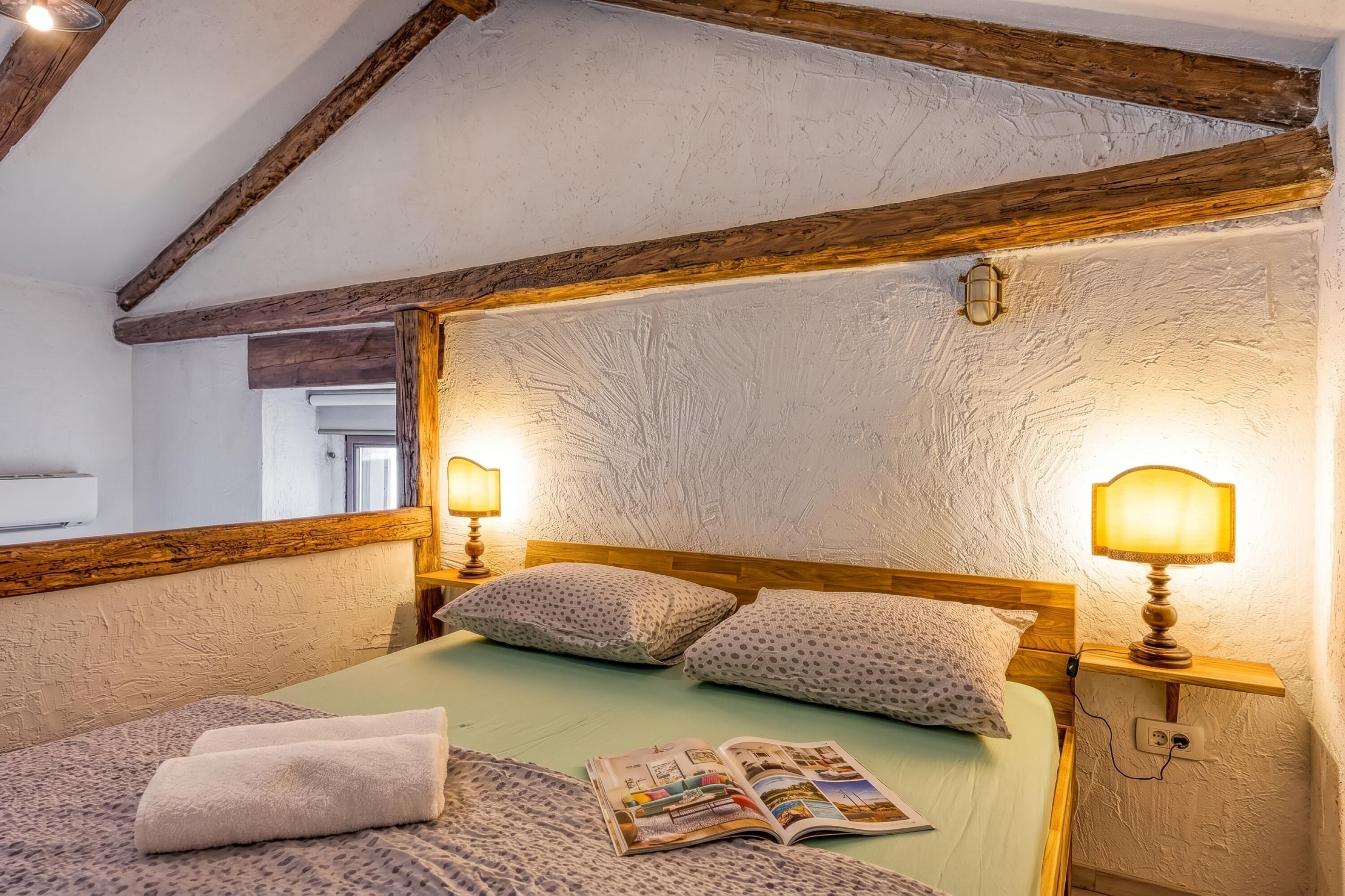 A bedroom with a wooden ceiling, two bedside lamps, a bed with a green bedspread, and a magazine on the bed.