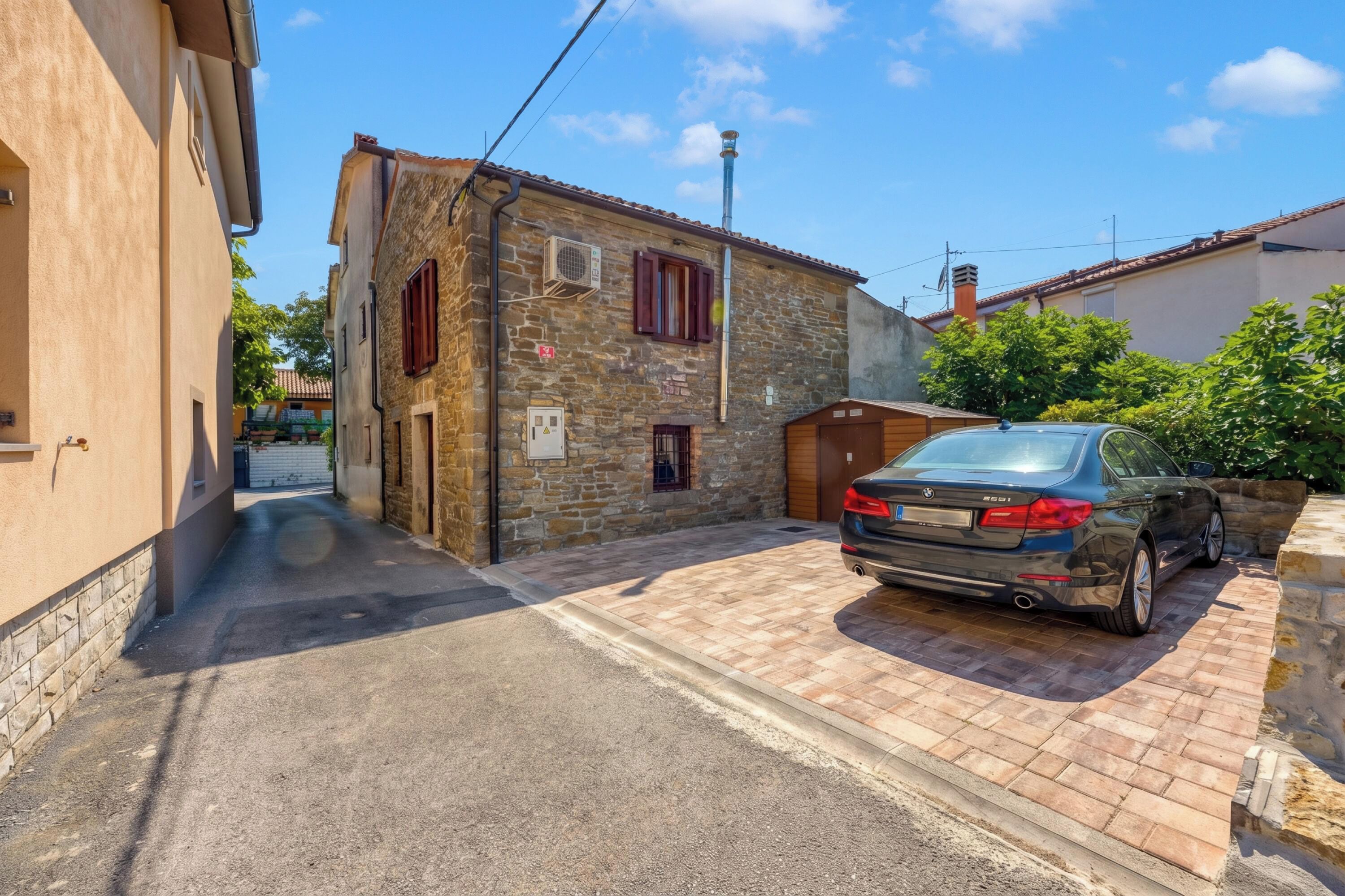 Une rue étroite, avec une voiture garée, des bâtiments en pierre et un ciel bleu dégagé.