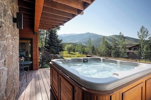 A hot tub on a wooden deck with a mountain view.