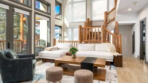 A modern living room with a sofa, coffee table, ottomans, and a staircase with wooden railings.