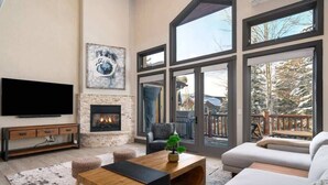 A spacious living room with a fireplace, large windows, a flat-screen TV, and a cozy seating area.