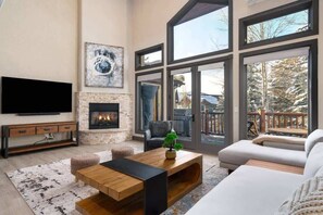 A spacious living room with a fireplace, large windows, a flat-screen TV, and a cozy seating area.