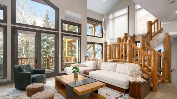 A spacious living room with a large window, a wooden staircase, and a cozy seating area.