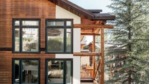 A modern log cabin with large windows, a wooden deck, and a view of a coniferous tree.