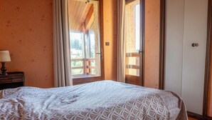 Une chambre à coucher comprenant un lit, une table de chevet, une fenêtre avec des rideaux et une porte donnant sur un espace extérieur.