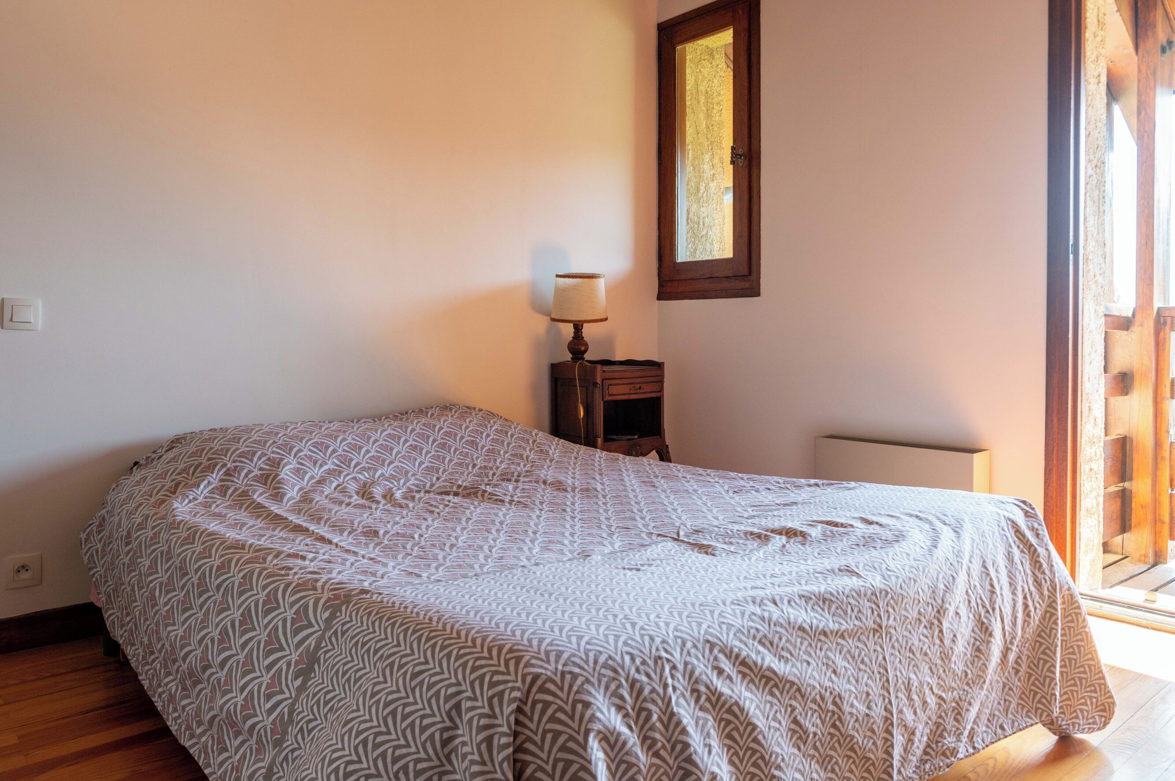 A bedroom with a patterned bedspread, a bedside table with a lamp, and a window with a view.