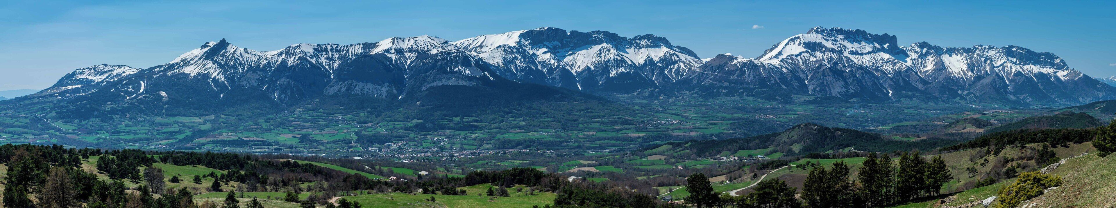 Un paysage de montagne avec des sommets enneigés et une vallée en contrebas.