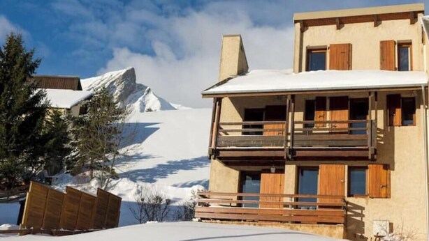 Un bâtiment à deux étages, doté de balcons en bois, avec un paysage enneigé en arrière-plan.