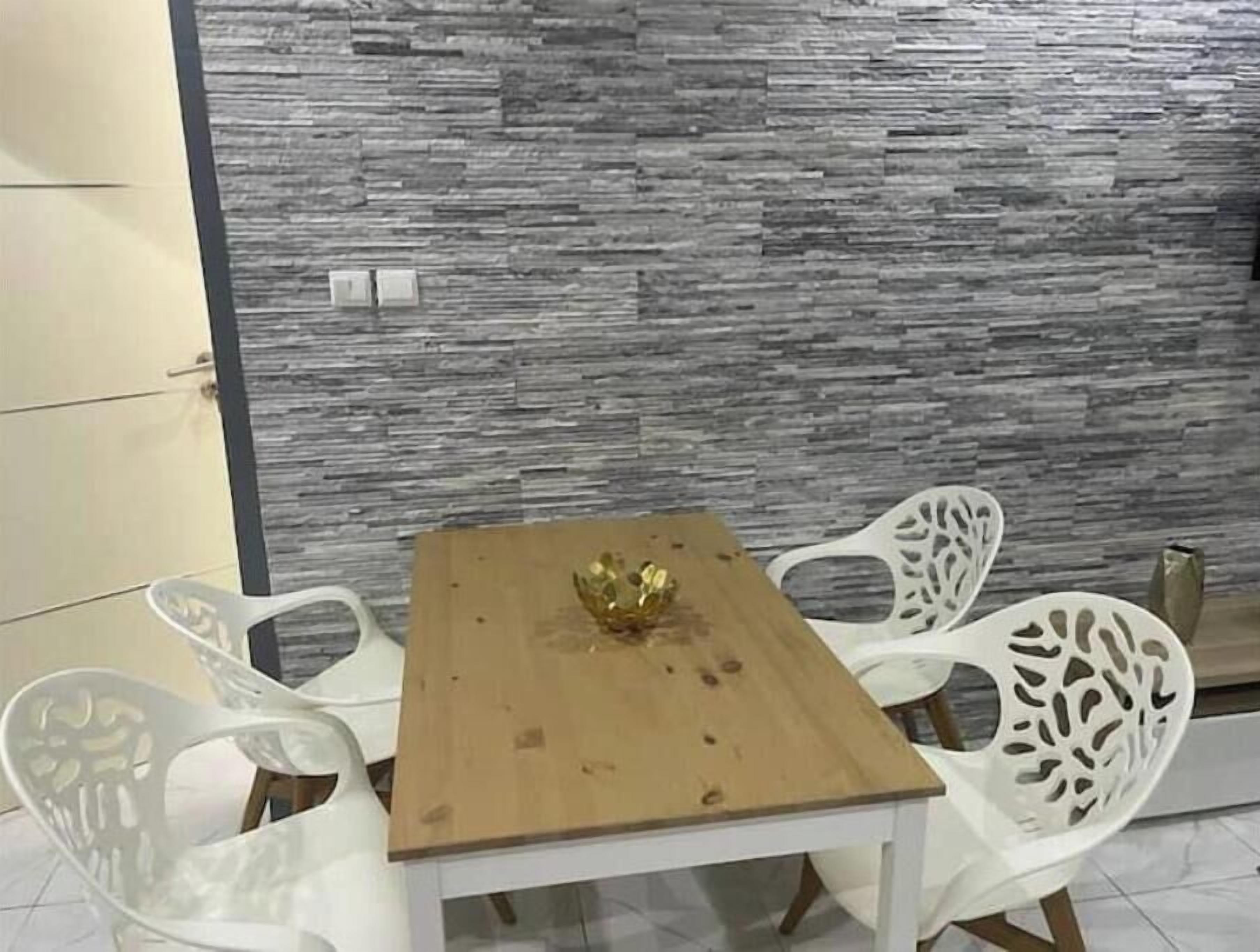 Ein Essbereich mit einem Holztisch und weißen Stühlen vor einer strukturierten Wand.