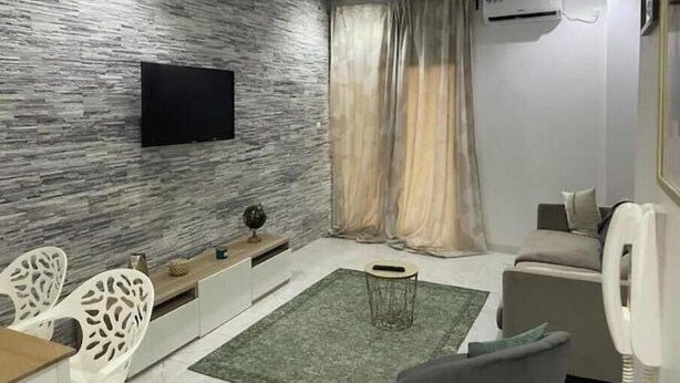 A modern living room with a stone-textured wall, a flat-screen TV, a sofa, and a dining area with chairs and a table. - Appartement Haut Standing à Dakar-résidence Mixta (Dakar)