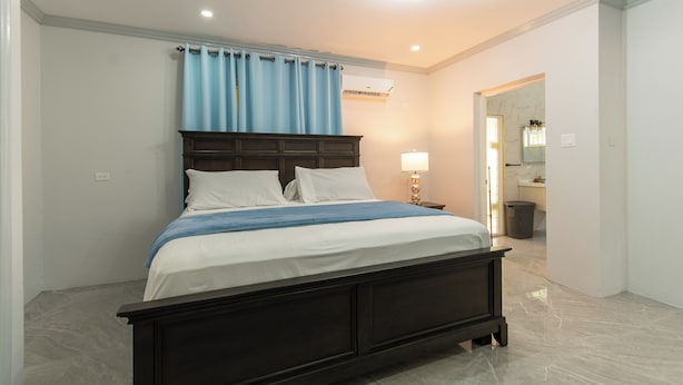 A bedroom with a large bed, a nightstand, a lamp, and a bathroom visible through an open door. - Cool Breeze at Secret Hideaway
Ocho Rios (Ocho Rios)
