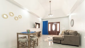 A living room with a sofa, a dining table with stools, a TV, and a door with curtains. - Cool Breeze at Secret Hideaway
Ocho Rios (Ocho Rios)