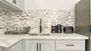 A modern kitchen with white cabinets, a tiled backsplash, a sink, a coffee maker, and a toaster. - Cool Breeze at Secret Hideaway
Ocho Rios (Ocho Rios)