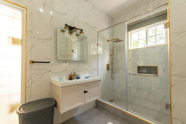 A modern bathroom with a glass-enclosed shower, a marble vanity, and a large mirror.