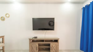 A room with a flat-screen TV mounted on a wooden TV stand, a small table, and a blue curtain. - Cool Breeze at Secret Hideaway
Ocho Rios (Ocho Rios)