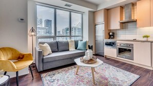 A modern apartment with a grey sofa, yellow armchair, and a city view through large windows.