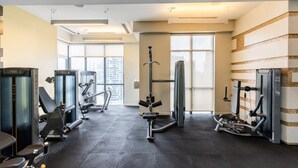 A modern gym with various exercise machines, large windows, and a tiled floor.