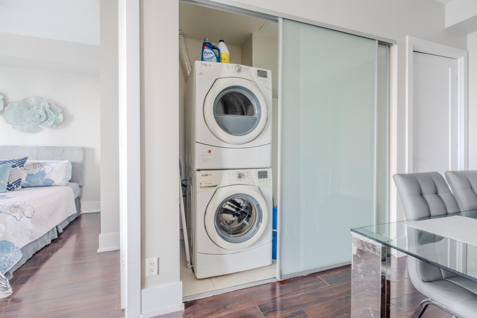 Un apartament modern amb rentadora i assecadora integrades, taula de dinar de vidre i llit amb roba de llit floral.