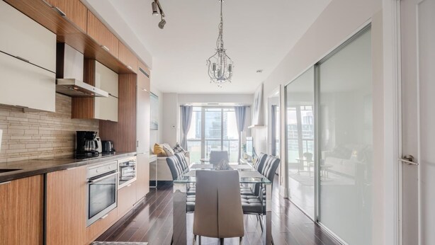 A modern kitchen with wooden cabinets, a dining area with a glass table, and a view of the city through large windows. - GLOBALSTAY. High Floor 1 Br in the Heart of DT (Toronto/Canada)