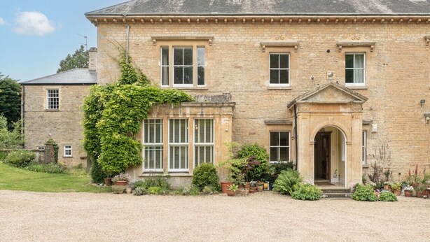 A stone building with a symmetrical facade, a central entrance with an arch, and a gravel driveway. - Gorgeous 3BD in Oxfordshire - Stunning Countryside (Steeple Aston)