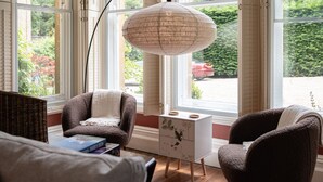 A cozy room with two armchairs, a small side table, and a large window with a view of greenery and a red car outside. - Gorgeous 3BD in Oxfordshire - Stunning Countryside (Steeple Aston)