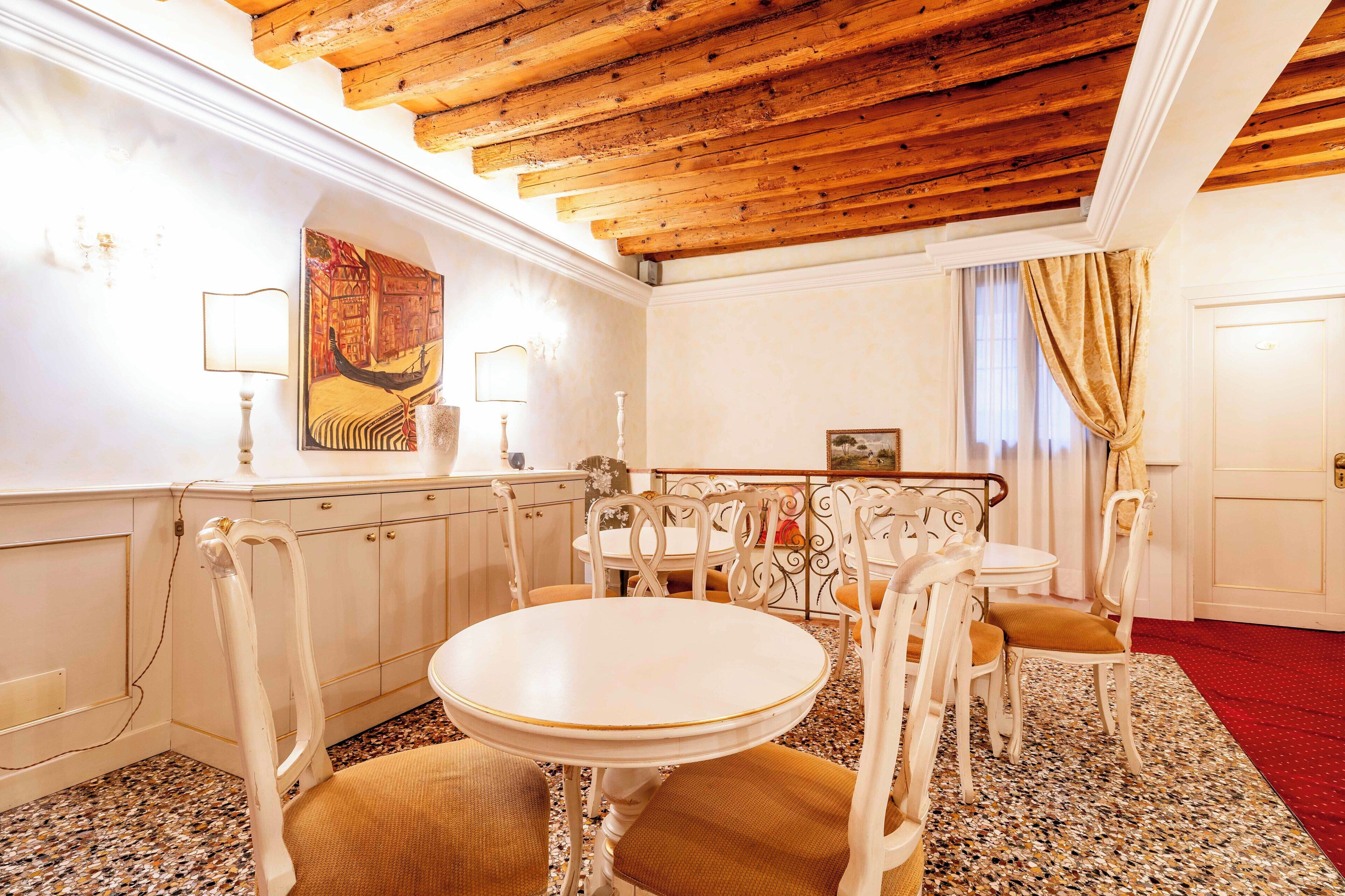 A dining area with a round table and chairs, a wooden ceiling, and a red carpet.