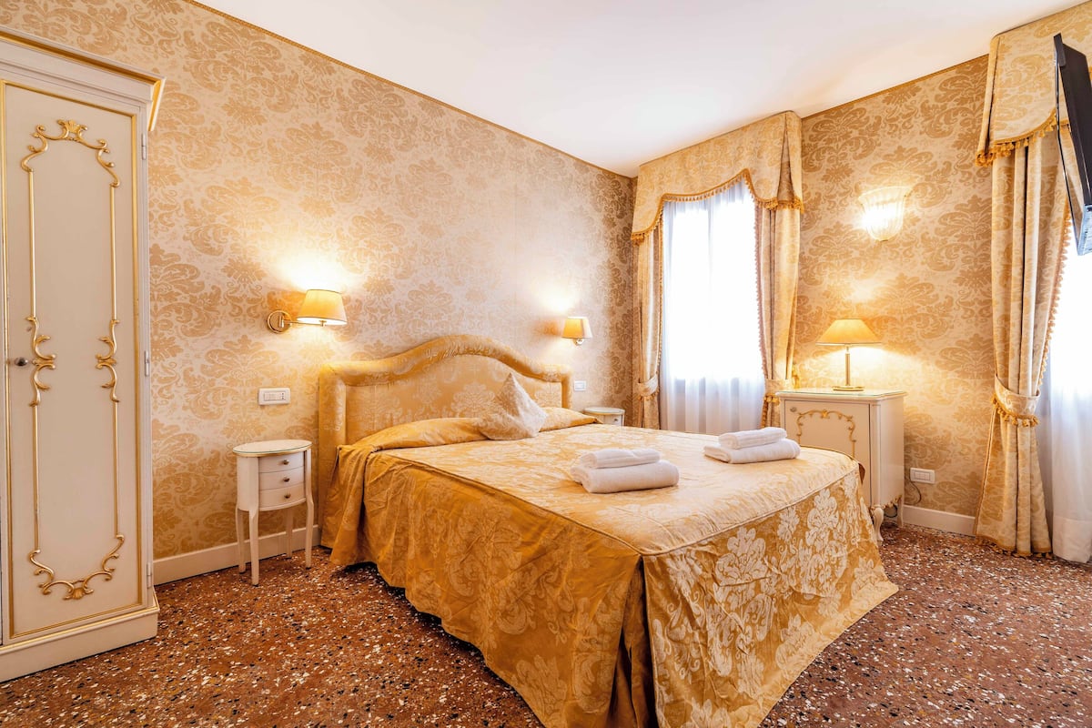 A room with a bed, two bedside tables, a wardrobe, and a wall-mounted lamp.
