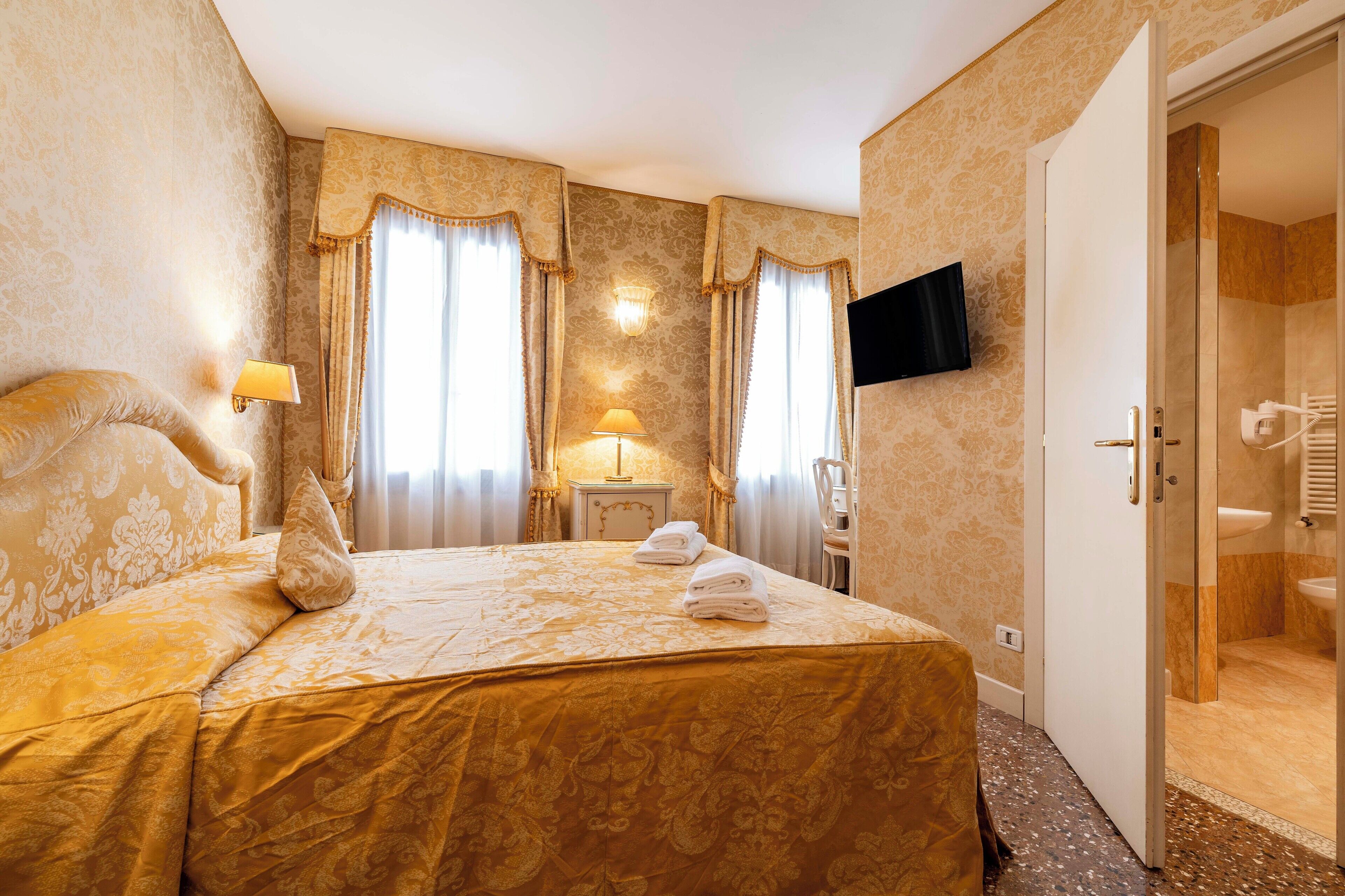 Une chambre d’hôtel avec un grand lit, deux lampes de chevet, un téléviseur à écran plat et une salle de bain visible à travers une porte ouverte.