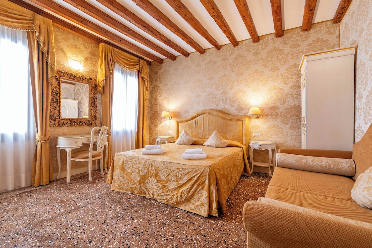 A hotel room with a bed, a desk, a chair, and a sofa.