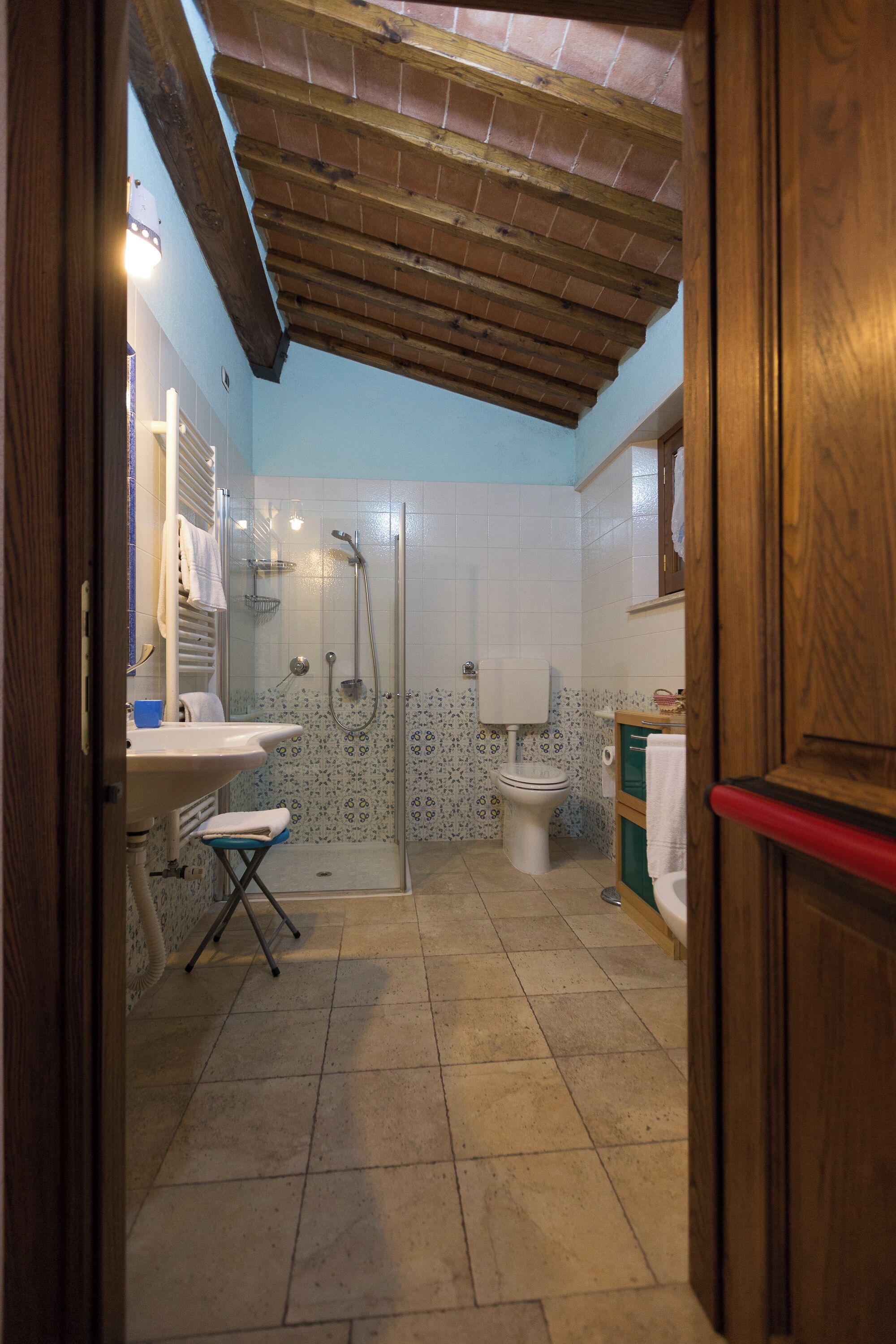 Un baño con ducha, inodoro, lavabo y un taburete pequeño.