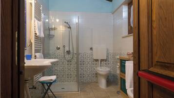 Un baño con ducha, inodoro, lavabo y un taburete pequeño.