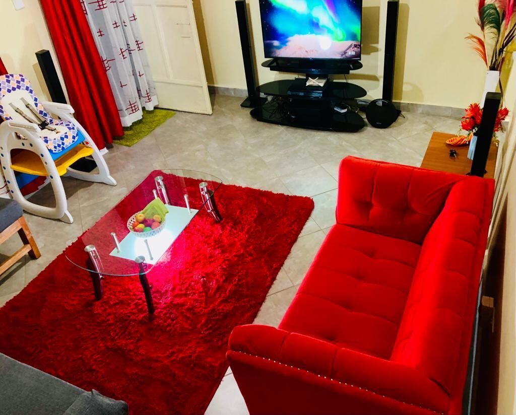 A living room with a red sofa, a glass coffee table with fruits, a TV, and a red rug.